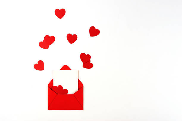 Red envelope with message note on white background, decorated with themed red confetti in the shape of heart. Valentine's day concept stock photo