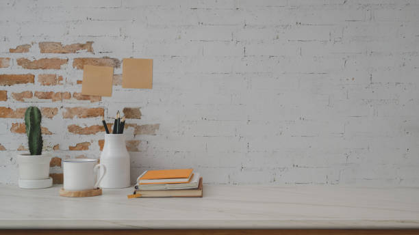 istock Cropped shot of  workspace with books, coffee cup, ceramic decorations and copy space on marble desk with brick wall 1200659936