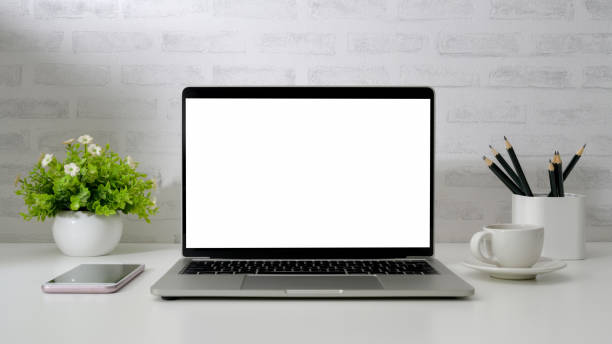 istock Close up view of workspace with blank screen laptop, smartphone, pencils, coffee cup and tree pot on white desk with  brick wall 1200660539