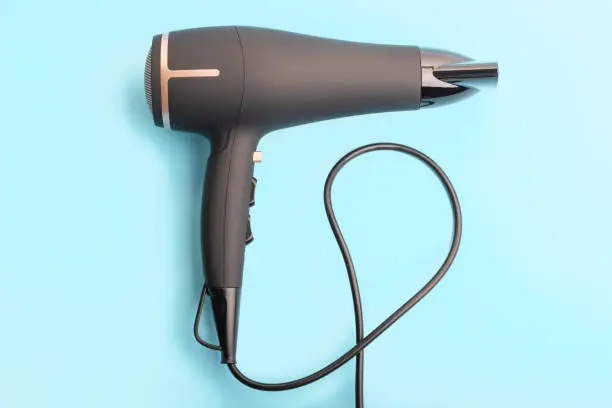 Black hair dryer on a blue background close up top view.