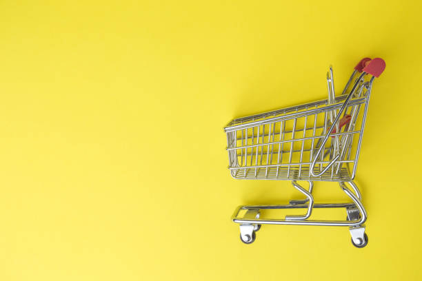 istock Shopping trolley toy on pastel yellow background. Space for copy. 1200663182