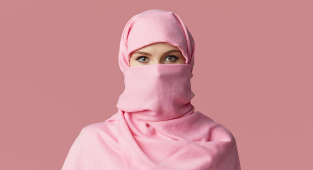 retrato de joven musulmana árabe con hiyab colorido sobre fondo rosa. apunta dedo a lado. espacio para texto - nikab veil islam arabia fotografías e imágenes de stock