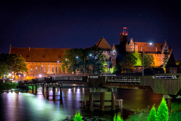 Malbork, Poland - July 27, 2019:Wooden bridge on the Nogat River in front of the medieval Malbork Castle by night, Poland. The largest castle in the world by surface area, and the largest brick building in Europe. Historical capitol of the Teutonic Order - Crusaders
