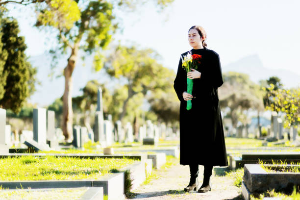 istock Young woman in black carrying flowers on cemetery path 1200671817