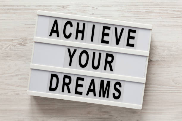 istock 'Achieve your dreams' words on a lightbox on a white wooden surface, top view. Overhead, from above, flat lay. 1200674056