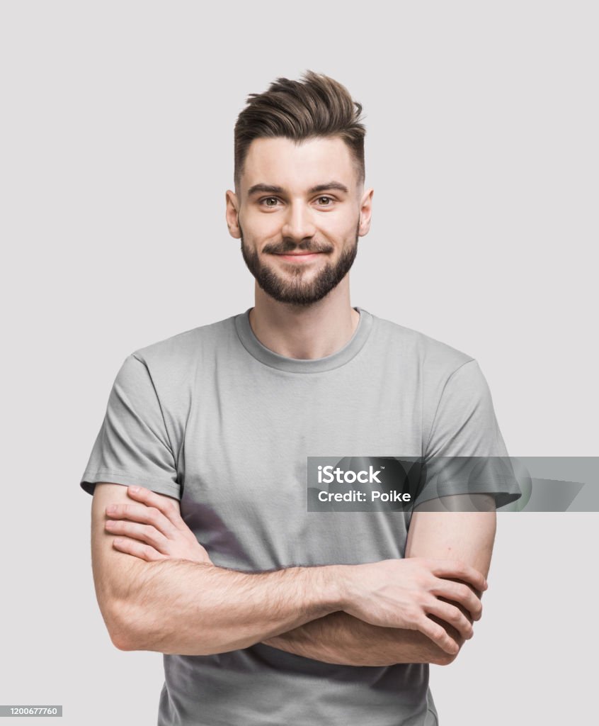Portrait of handsome smiling young man with crossed arms Cheerful young man with crossed hands looking to the camera. Isolated on gray background Men Stock Photo