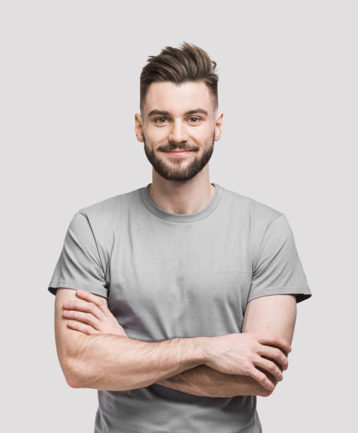 Portrait of handsome smiling young man with crossed arms Cheerful young man with crossed hands looking to the camera. Isolated on gray background portrait stock pictures, royalty-free photos & images