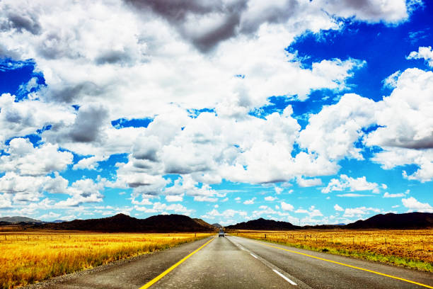 A country road runs through farmland under a lightly clouded sky.