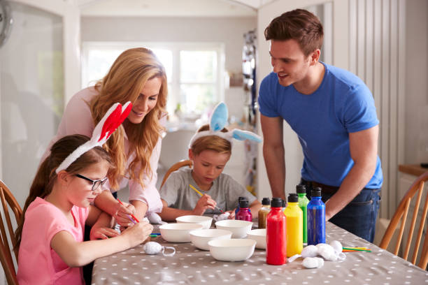 istock Parents With Children Wearing Bunny Ears Sitting At Table Decorating Eggs For Easter At Home 1200678801