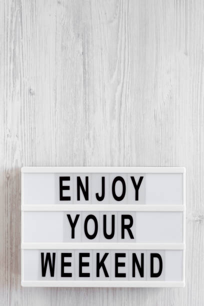 istock 'Enjoy your weekend' words on a lightbox on a white wooden surface, top view. Overhead, from above, flat lay. Copy space. 1200679249