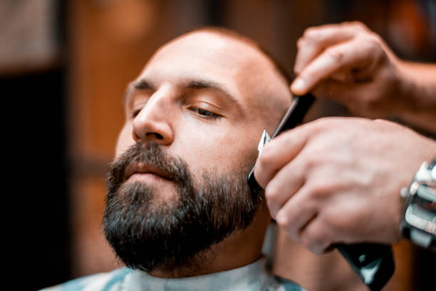 istock Young man getting his beard shaped by an electric trimmer in a barber shop 1200679610