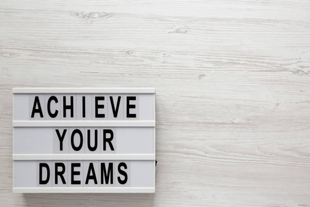 istock 'Achieve your dreams' words on a lightbox on a white wooden surface, top view. Overhead, from above, flat lay. Copy space. 1200680221