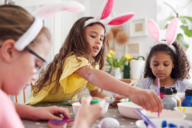 istock Three Girls Wearing Bunny Ears Sitting At Table Decorating Eggs For Easter At Home 1200680253