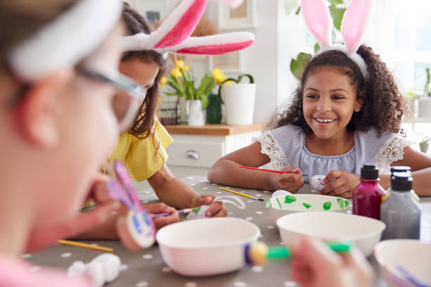 istock Three Girls Wearing Bunny Ears Sitting At Table Decorating Eggs For Easter At Home 1200680509