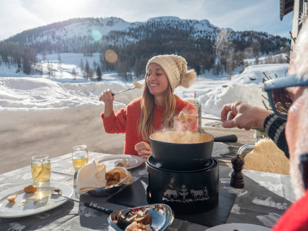 Family eating Swiss cheese fondue in the Alps in winter Two people sharing meeting cheese fondue outside chalet enjoying traditional food. chalet stock pictures, royalty-free photos & images