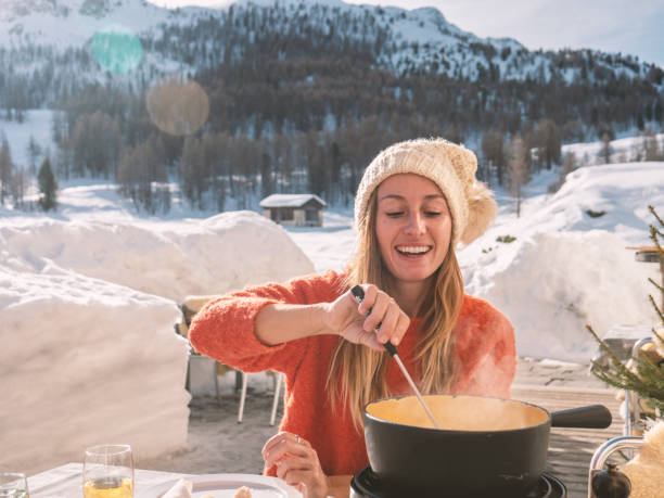 молодая женщина ест сыр фондю в шале - fondue swiss culture winter cheese стоковые фото и изображения