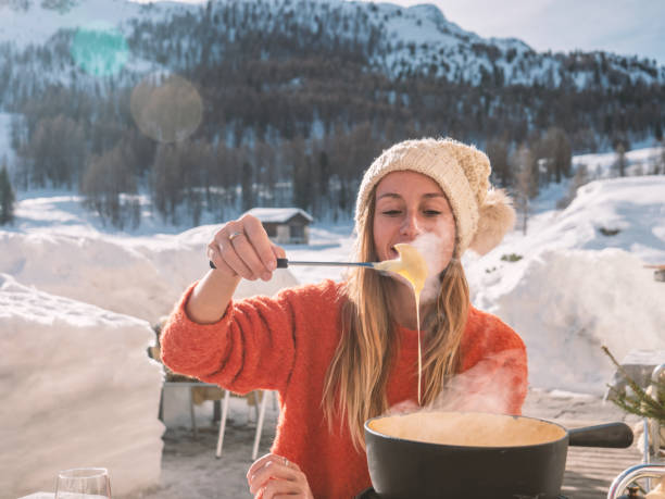 jeune femme mangeant la fondue de fromage dans le chalet - fondue swiss culture winter cheese photos et images de collection