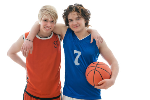 Two men posin in front of black wall with basketball.