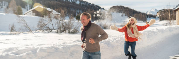 Women and men having snowball fight in snow on sunny day.