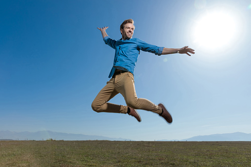 gorgeous casual man wearing blue shirt jumping high to the blue sky outdoor
