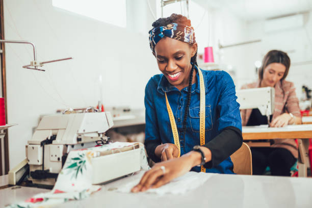 Dressmaker woman working with sewing machine Young african textile worker sewing on production line. Dressmaker woman working with sewing machine woman tailor stock pictures, royalty-free photos & images