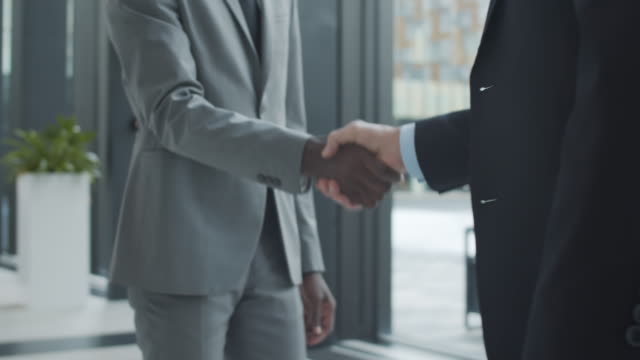 Unrecognizable Multiethnic Businessmen Shaking Hands in Office Hallway