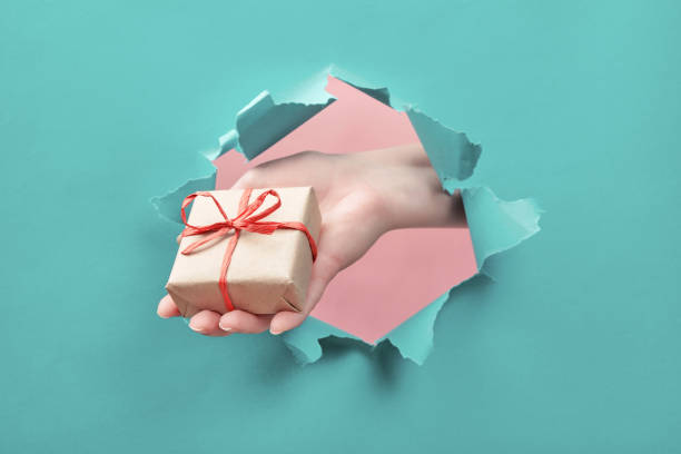 istock Hand holds a craft gift through a torn paper hole. Special offer, sale, bonus, present 1200699310