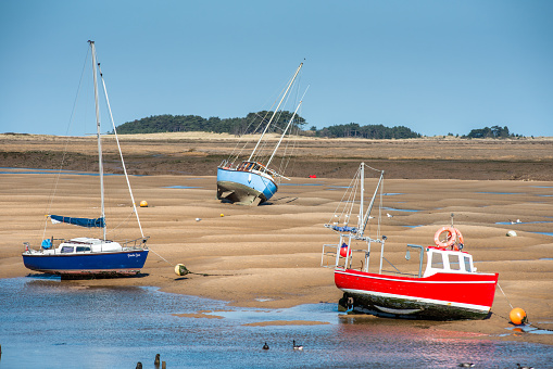 Colourful boats marooned on sandbanks at low tide on East Fleet river estuary at Wells next the sea, North Norfolk coast, East Anglia, England, UK.