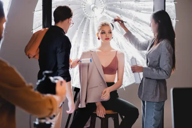Photo of selective focus of stylist using lint roller and hairstylist doing hairstyle to stylish model on backstage