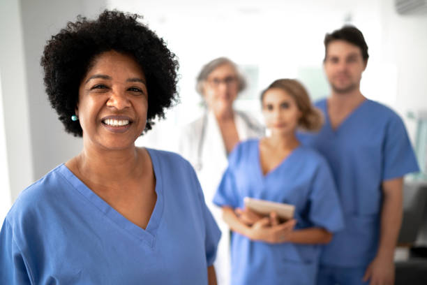 Portrait of female mature nurse with team on background at hospital Portrait of female mature nurse at hospital female nurse photos stock pictures, royalty-free photos & images