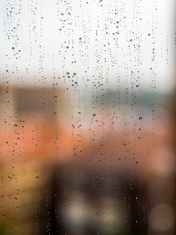 Rain water from the outside streaking down a window pane, forming well defined beads in the process. Background defocussed.
