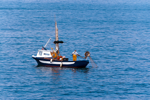 Gulf of La Spezia, Liguria, Italy - July 29th, 2011: one senior fisherman on a small blue and white boat with fishing net between the waves of the Mediterranean sea. Liguria, Italy, Europe