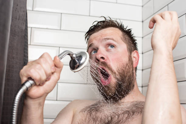 carino uomo barbuto che canta in bagno usando il soffione della doccia con acqua che scorre invece di un microfono. - tenor foto e immagini stock