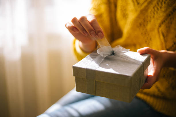 young woman in yellow sweater opening gift box - gift imagens e fotografias de stock