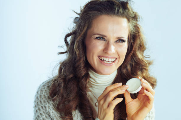 istock smiling woman applying lip balm on winter light blue background 1200709603