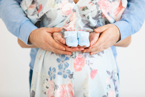 joven embarazada sostiene botines de bebé frente a su vientre - gender reveal - party newborn baby hospital fotografías e imágenes de stock