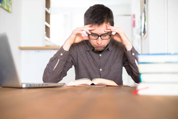 learning and studying concept: young exhaust and unhappy male student is learning at home, stack of books - overstrained imagens e fotografias de stock