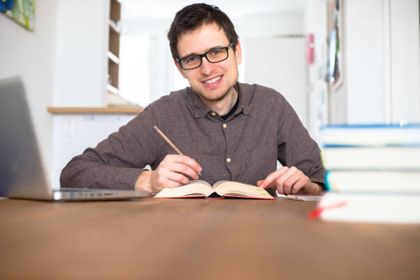 istock Learning and studying concept: Young happy male student is learning at home, stack of books 1200713525