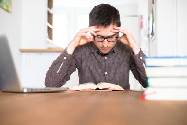 learning and studying concept: young exhaust and unhappy male student is learning at home, stack of books - overstrained imagens e fotografias de stock