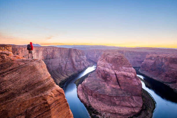 Male hiker overlooking Horseshoe Bend at sunset, Arizona, USA A male hiker is standing on steep cliffs enjoying the beautiful view of Colorado river flowing at famous Horseshoe Bend overlook in beautiful post sunset twilight on a summer evening, Arizona, USA horseshoe bend river stock pictures, royalty-free photos & images