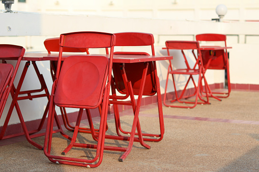 Foldable red table and chair set placed outdoors. Foldable chairs, leaning on the table. Temporary table and chair set placed outdoors. Red eatery table and chairs set.