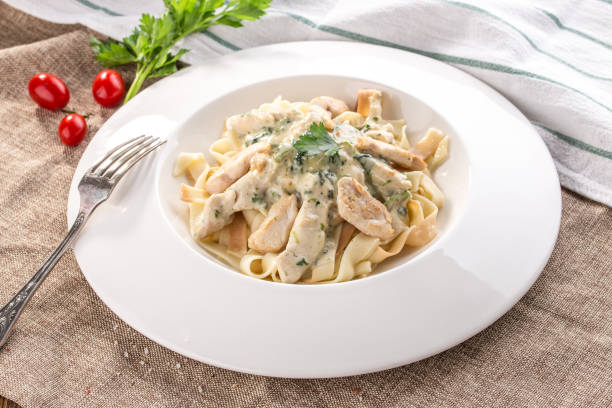 fettuccine pasta with chicken and cheese sauce on white plate on tablecloth stock photo