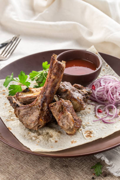 istock Grilled lamb ribs on lavash bread with red onion and tomato sauce on tablecloth 1200721782