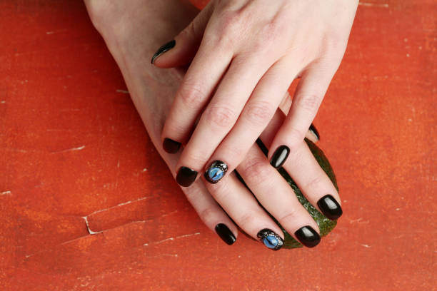 istock Dark nail art on manicured hands on red background 1200725313