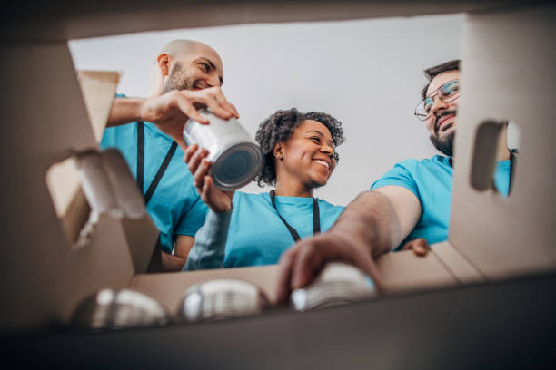 diversos voluntarios empacando cajas de donación con alimentos enlatados en banco de alimentos - caridad y auxilio fotografías e imágenes de stock