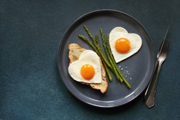 ovos fritos em forma de coração em prato azul. - eggs breakfast heart shape fried egg - fotografias e filmes do acervo