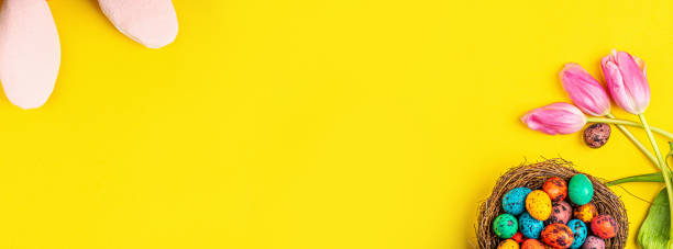 istock Stylish background with colorful easter eggs isolated on yellow background with pink tulip flowers. Flat lay, top view, mockup, overhead, template 1200729989