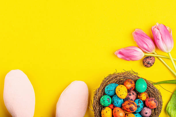 istock Stylish background with colorful easter eggs isolated on yellow background with pink tulip flowers. Flat lay, top view, mockup, overhead, template 1200730261