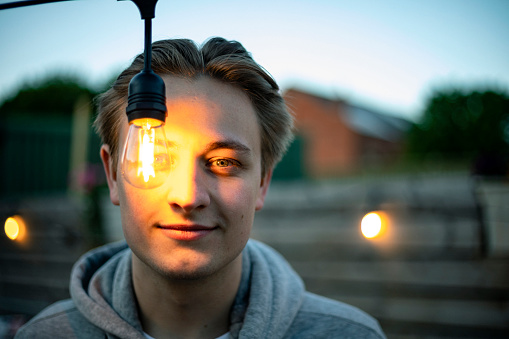 A front-view shot of a young man looking at a lightbulb, he has taught of an idea.