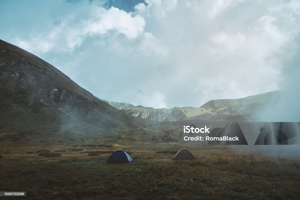 Camping in the mountains Tent on the hill beneath the mountains under dramatic sky Adventure Stock Photo
